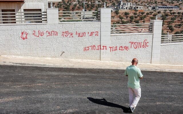Un homme passant devant un graffiti israélien disant « Al-Mughayyir, tu le regretteras », après une attaque d'Israéliens radicaux contre le village chrétien de Taybeh, au nord-est de Ramallah, en Cisjordanie, le 28 juillet 2025. (Crédit : Zain Jaafar/AFP) Un homme passant devant un graffiti israélien disant « Al-Mughayyir, tu le regretteras », après une attaque d'Israéliens radicaux contre le village chrétien de Taybeh, au nord-est de Ramallah, en Cisjordanie, le 28 juillet 2025. (Crédit : Zain Jaafar/AFP)
