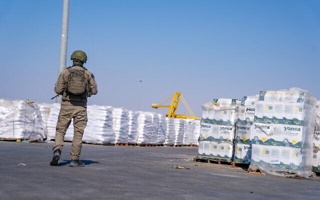 Un soldat se tient près de colis d'aide humanitaire du côté gazan du point de passage de Kerem Shalom, dans le sud de la bande de Gaza, le 24 juillet 2025. (Crédit : Emanuel Fabian/Times of Israel)