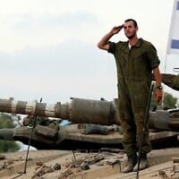 Image d'illustration : un soldat israélien sur un char salue devant un drapeau israélien à un point de rassemblement de Tsahal dans un champ, près de la frontière israélienne avec Gaza, 2014. (Crédit : Edi Israel/FLASH90)
