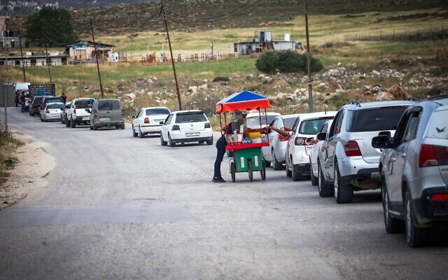 Des Palestiniens achetant des boissons à un vendeur ambulant alors qu'ils attendent à un poste de contrôle israélien, près de Naplouse, le 1ᵉʳ mai 2025. (Crédit : Nasser Ishtayeh/Flash90)