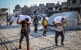 Des Gazaouis marchant dans les rues avec des sacs de farine après l'arrivée de camions d'aide humanitaire via le passage de Kerem Shalom, contrôlé par Israël, dans le sud de Gaza, à Khan Younès, le 24 juillet 2025. (Crédit : Abed Rahim Khatib/Flash90)