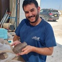Dudu Biton, de l'Autorité israélienne des antiquités, tient un noyau de silex destiné à la fabrication de lames cananéennes trouvées à Nahal Qomem, près de Kiryat Gat, lors d'une découverte rendue publique en juillet 2025. (Crédit : Shira Lifshitz/Autorité israélienne des antiquités)