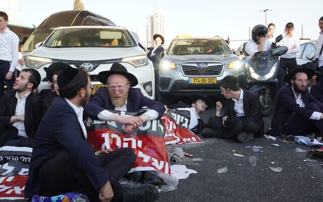 Des manifestants haredim protestant contre les efforts visant à enrôler les étudiants en yeshiva dans l'armée israélienne à l'entrée de Jérusalem, le 23 juillet 2025. (Crédit : Charlie Summers/Times of Israel)