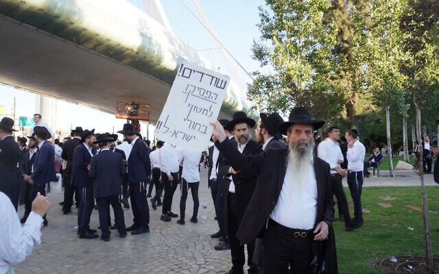 Un manifestant haredi brandissant une pancarte sur laquelle on peut lire : « Bandits, arrêtez d'enlever les jeunes hommes d'Israël ! » lors d'une manifestation contre la conscription obligatoire dans l'armée israélienne des ultra-orthodoxes, à Jérusalem, le 23 juillet 2025. (Crédit : Charlie Summers/Times of Israel)