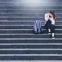 Illustration : Une élève bouleversée assise dans la cour d'une école. (Crédit : iStock par Getty Images)