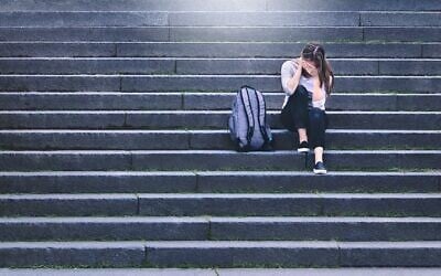 Illustration : Une élève bouleversée assise dans la cour d'une école. (Crédit : iStock par Getty Images)