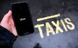 Illustration : Un homme tenant un smartphone où figure l'application du service de covoiturage Uber, à Londres, le 17 mars 2021. (Crédit : Tolga Akmen/AFP)