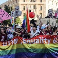 Des participants brandissant des silhouettes représentant des responsables politiques israéliens hostiles à la communauté LGBTQ+ ainsi qu'un drapeau arc-en-ciel géant sur lequel figurent les mots « égalité » et « paix » en hébreu, en anglais et en arabe, dans le centre-ville de Jérusalem à l'occasion de la Gay Pride annuelle de la capitale, le 5 juin 2025. (Crédit : Ahmad Gharabli/AFP)