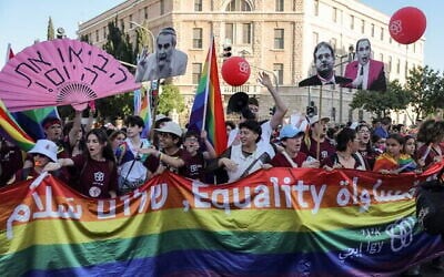 Des participants brandissant des silhouettes représentant des responsables politiques israéliens hostiles à la communauté LGBTQ+ ainsi qu'un drapeau arc-en-ciel géant sur lequel figurent les mots « égalité » et « paix » en hébreu, en anglais et en arabe, dans le centre-ville de Jérusalem à l'occasion de la Gay Pride annuelle de la capitale, le 5 juin 2025. (Crédit : Ahmad Gharabli/AFP)