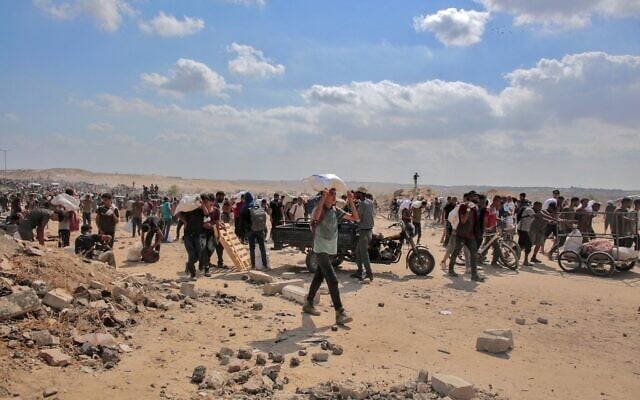 Des Gazaouis déplacés transportant des sacs d'aide humanitaire qu'ils ont reçus dans un centre de distribution géré par la Fondation humanitaire de Gaza (GHF), soutenue par les États-Unis et Israël, dans le centre de la bande de Gaza, le 4 août 2025. (Crédits : AFP)