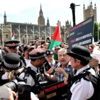 Des policiers discutent avec un manifestant pendant une manifestation pour soutenir le groupe interdit Palestine Action, sur Parliament Square, dans le centre de Londres, le 9 août 2025. (Crédit : HENRY NICHOLLS / AFP)