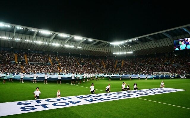 Des mascottes brandissant une banderole sur laquelle on peut lire « Arrêtez de tuer des enfants, arrêtez de tuer des civils » sur le terrain avant la finale de la Supercoupe de l'UEFA 2025, au stade Friuli, à Udine, en Italie, le 13 août 2025. (Crédit : Marco Bertorello/AFP)