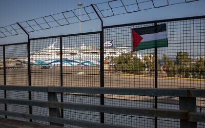Un drapeau palestinien accroché par des manifestants sur une clôture du port du Pirée lors d'une manifestation contre l'arrivée du « Crown Iris » (à l'arrière-plan), un paquebot transportant des touristes israéliens à Athènes, le 14 août 2025. (Crédit : Angelos TZORTZINIS / AFP)
