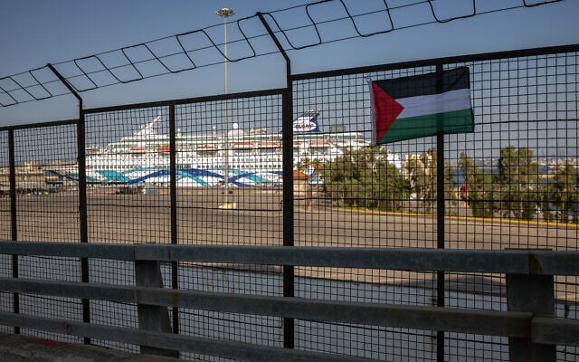 Un drapeau palestinien accroché par des manifestants sur une clôture du port du Pirée lors d'une manifestation contre l'arrivée du « Crown Iris » (à l'arrière-plan), un paquebot transportant des touristes israéliens à Athènes, le 14 août 2025. (Crédit : Angelos TZORTZINIS / AFP)