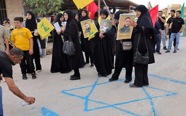 Des partisans du groupe terroriste chiite libanais du Hezbollah sur un graffiti représentant une étoile de David lors d'une manifestation contre la visite prévue de l'envoyé américain Tom Barrack dans le sud du Liban, à Khiam, le 27 août 2025. (Crédit : Rabih Daher/AFP) Des partisans du groupe terroriste chiite libanais du Hezbollah sur un graffiti représentant une étoile de David lors d'une manifestation contre la visite prévue de l'envoyé américain Tom Barrack dans le sud du Liban, à Khiam, le 27 août 2025. (Crédit : Rabih Daher/AFP)