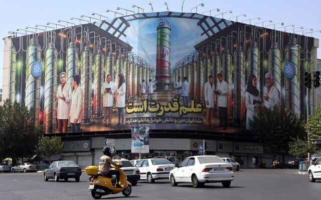 Des Iraniens passant devant un panneau d'affichage montrant des photos de scientifiques nucléaires, de centrifugeuses et une phrase en farsi : "La science est le pouvoir" sur la place Enqelab à Téhéran, le 29 août 2025 (Crédit : AFP)