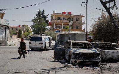 Illustration : Un milicien druze armé d'une mitrailleuse passant devant une voiture incendiée, à la suite d'affrontements religieux dans la ville à majorité druze de Soueïda, en Syrie, le 25 juillet 2025. (Crédit : Omar Sanadiki/AP Photo)