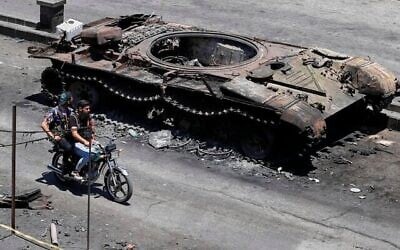Des miliciens druzes passent à moto devant un véhicule militaire détruit lors d'affrontements religieux la semaine dernière dans la ville à majorité druze de Sweida, en Syrie, le 25 juillet 2025. (Crédit : AP Photo/Omar Sanadiki)