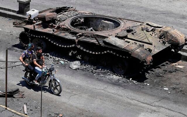 Des miliciens druzes passent à moto devant un véhicule militaire détruit lors d'affrontements religieux la semaine dernière dans la ville à majorité druze de Sweida, en Syrie, le 25 juillet 2025. (Crédit : AP Photo/Omar Sanadiki)