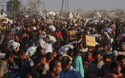 Des Palestiniens transportent des colis alimentaires provenant d'un convoi humanitaire ayant emprunté le corridor de Morag près de Rafah, dans le sud de la bande de Gaza, le 4 août 2025. (Crédit : AP Photo/Mariam Dagga)