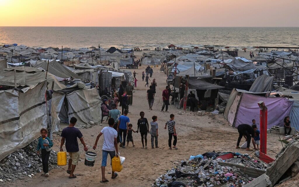 Des Palestiniens déplacés marchent dans un camp de fortune le long de la plage de Gaza-City, le 10 août 2025. (Crédit : Jehad Alshrafi/AP) Des Palestiniens déplacés marchent dans un camp de fortune le long de la plage de Gaza-City, le 10 août 2025. (Crédit : Jehad Alshrafi/AP)