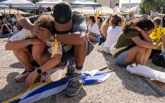 Des personnes s'assoient par terre et se couvrent la tête alors que des sirènes annoncent l'arrivée d'un missile tiré depuis le Yémen lors d'une manifestation exigeant la libération immédiate des otages détenus par le Hamas, à Tel-Aviv, le 17 août 2025. (Crédit : AP Photo/Maya Levin)