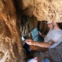 Le Dr Asaf Gayer, du département d'études sur la terre d'Israël et d'archéologie de l'université d'Ariel, examine une grotte près du parc national d'Ein Gedi, dans la région de la mer Morte, où se trouve une ancienne inscription en araméen, datant peut-être de la révolte de Bar Kochba, qui a été révélée au grand public en août 2025. (Crédit : Asaf Gayer)