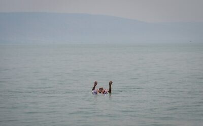 Un Israélien se laisse flotter sur le lac de Tibériade au milieu d'une vague de chaleur, le 14 août 2025. (Crédit : Michael Giladi/Flash90)
