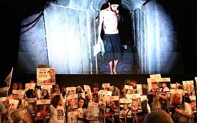 Des manifestants brandissant des affiches représentant les otages devant une image tirée d'une vidéo du Hamas montrant l'otage Evyatar David, le 2 août 2025. (Crédit : Paulina Patimer/Forum des familles des otages et disparus)