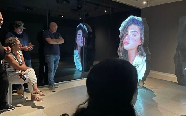 Des visiteurs lors du vernissage de l'exposition « Renaître de ses cendres : l'archéologie au coeur d'une crise nationale », sur le campus Jay et Jeanie Schottenstein de l'Autorité des antiquités d'Israël à Jérusalem, le 5 août 2025. L'installation multimédia présente une photo de Shani Gabay,  victime du 7 octobre identifiée grâce au travail de l'Autorité des antiquités d'Israël. (Crédit : Rossella Tercatin/Times of Israel)