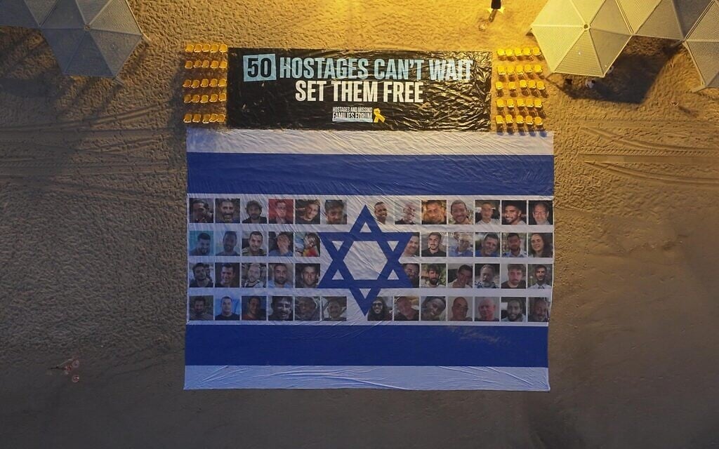 Un grand drapeau d'Israël avec les photos des 50 otages restants déployé devant l'ambassade américaine à Tel Aviv, à côté d'une banderole réclamant un accord pour leur libération, le 26 août 2025. (Crédit : Aviv Atlas/Mouvement de protestation israélien pour la démocratie)