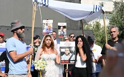 Ilana Gritzewsky (au centre), John Polin (à gauche) et Einav Zangauker (à droite) organisant un mariage symbolique entre Ilana et son petit ami Matan Zangauker, toujours retenu captif à Gaza, le 17 août 2025, sur la Place des Otages, à Tel Aviv. (Crédit : Paulina Patimer/Forum des familles des otages et disparus) Ilana Gritzewsky (au centre), John Polin (à gauche) et Einav Zangauker (à droite) organisant un mariage symbolique entre Ilana et son petit ami Matan Zangauker, toujours retenu captif à Gaza, le 17 août 2025, sur la Place des Otages, à Tel Aviv. (Crédit : Paulina Patimer/Forum des familles des otages et disparus)