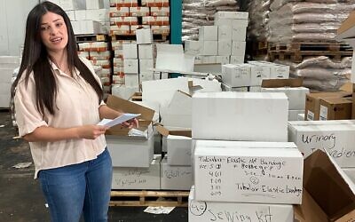 Najwa Mulla, une bénévole, se tient dans un entrepôt du village druze de Julis, en Galilée, à côté de cartons de fournitures médicales qui seront envoyés à des hôpitaux de Soueïda, en Syrie, le 6 août 2025. (Crédit : Diana Bletter/Times of Israel)