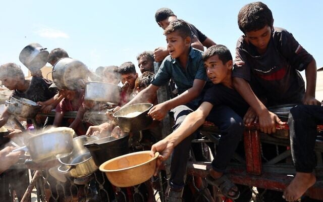 Des Gazaouis attendant de recevoir du riz cuit dans leurs casseroles vides, dans une cuisine communautaire, à Gaza-City, le 23 août 2025. (Crédit : Omar al-Qattaa/AFP) Des Gazaouis attendant de recevoir du riz cuit dans leurs casseroles vides, dans une cuisine communautaire, à Gaza-City, le 23 août 2025. (Crédit : Omar al-Qattaa/AFP)