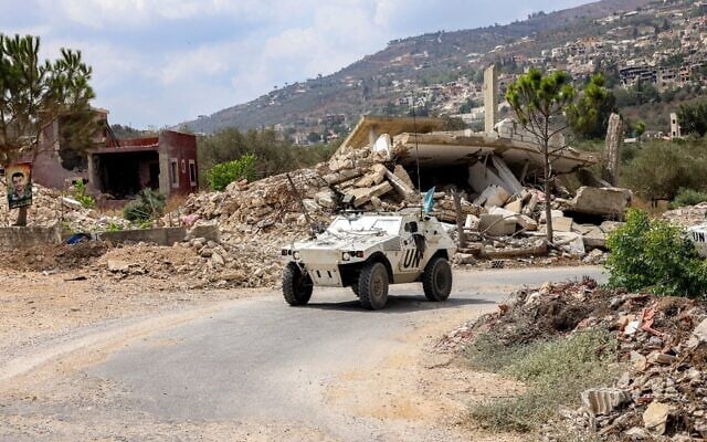Un véhicule blindé de la Force intérimaire des Nations unies au Liban (FINUL) passe devant des bâtiments détruits le long d'une route dans le village de Kfar Kila, dans le sud du Liban, près de la frontière avec le nord d'Israël, le 27 août 2025. (Crédit : ANWAR AMRO / AFP)
