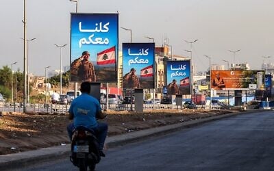 Un homme roule en scooter devant des panneaux représentant un soldat libanais saluant le drapeau national, accompagnés du slogan en arabe « Nous sommes tous avec vous », le long de l'autoroute menant à l'aéroport international de Beyrouth, dans le sud de Beyrouth, le 5 septembre 2025. (Crédit ; ANWAR AMRO / AFP)