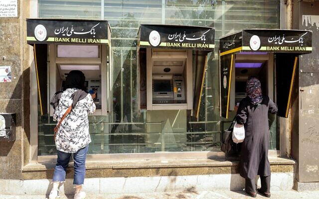 Des personnes retirent de l'argent à un distributeur automatique dans la capitale iranienne Téhéran, le 28 septembre 2025. (Crédit : ATTA KENARE / AFP)