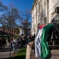 Des étudiants manifestent contre la guerre à Gaza, et des passants déambulent dans Harvard Yard, non loin de la statue de John Harvard, le premier bienfaiteur du Harvard College, drapé dans le drapeau palestinien, lors d'un campement de l'Université Harvard à Cambridge, dans le Massachusetts, le 25 avril 2024. (Crédit : AP Photo/Ben Curtis)