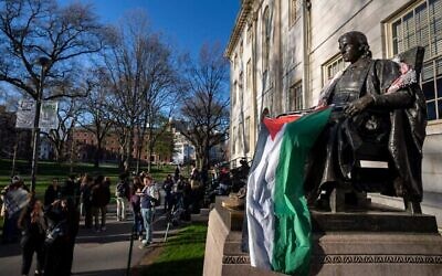 Des étudiants manifestent contre la guerre à Gaza, et des passants déambulent dans Harvard Yard, non loin de la statue de John Harvard, le premier bienfaiteur du Harvard College, drapé dans le drapeau palestinien, lors d'un campement de l'Université Harvard à Cambridge, dans le Massachusetts, le 25 avril 2024. (Crédit : AP Photo/Ben Curtis)