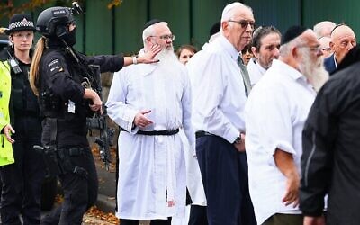 Le rabbin Daniel Walker (3ᵉ à gauche) parmi des policiers armés, discutant avec des membres de la communauté juive après une attaque terroriste meurtrière devant la synagogue de la Congrégation hébraïque de Heaton Park, à Crumpsall, au nord de Manchester, le 2 octobre 2025. (Crédit : Paul Currie/AFP)