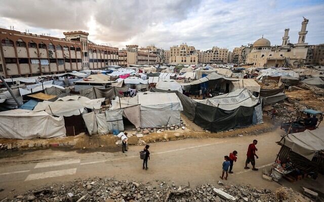 Des personnes passent devant des tentes abritant des Gazaouis déplacés près de la mosquée Sheikh Hamad bin Khalifa Al-Thani, dans le complexe résidentiel Hamad City construit par le Qatar au nord-ouest de Khan Younis, dans le sud de la bande de Gaza, le 6 octobre 2025. (Crédit : Omar Al-Qattaa/ AFP)