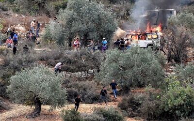 Des soldats de l'armée israélienne et un véhicule blindé se déploient (en haut à droite) tandis que des Palestiniens et des premiers intervenants tentent d'éteindre un véhicule incendié lors d'une attaque menée par des extrémistes israéliens contre des Palestiniens et d'autres militants qui s'étaient rassemblés pour la saison annuelle de la récolte des olives dans le village palestinien de Beita, au sud de Naplouse, en Cisjordanie, le 10 octobre 2025. (Crédit : Jaafar ASHTIYEH / AFP)