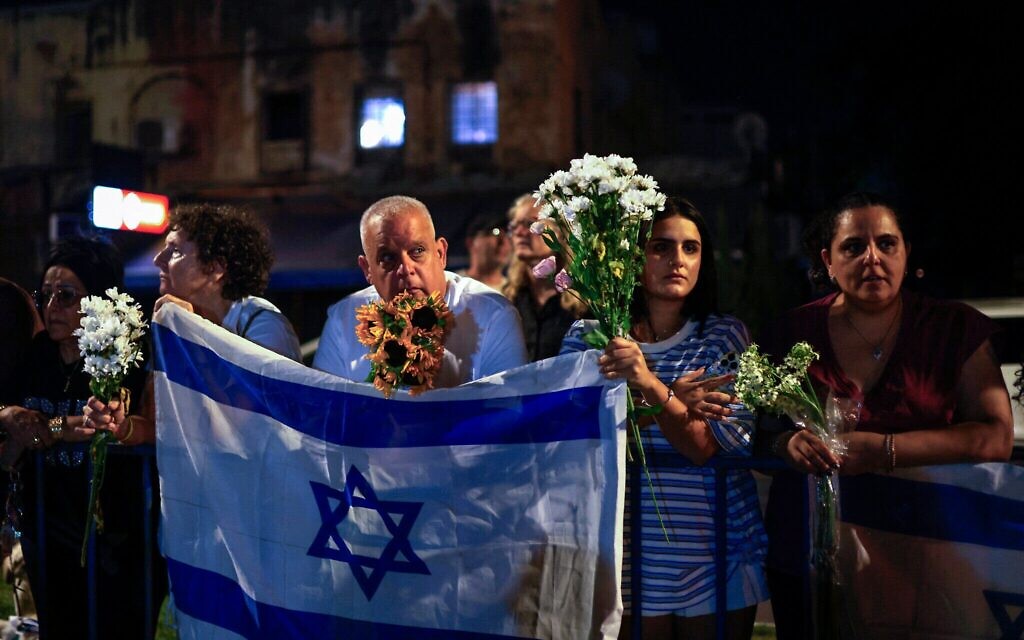 Des personnes portent des fleurs et des drapeaux israéliens à l'arrivée des véhicules transportant les corps des quatre otages, devant le Centre national de médecine légale à Tel Aviv, le 13 octobre 2025. (Crédit : Jalaa Marey/AFP)