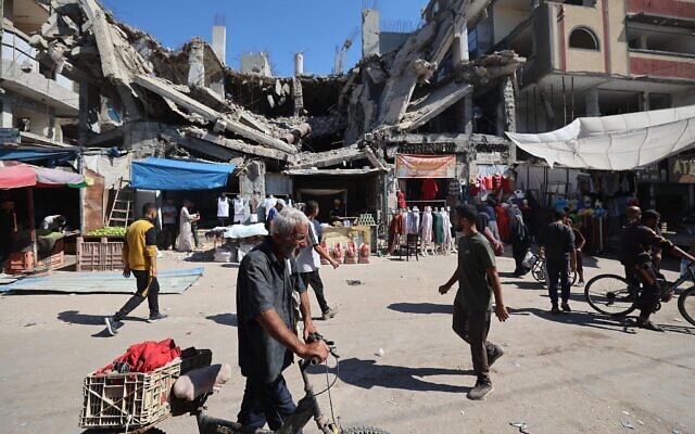 Des Gazaouis passant devant un bâtiment détruit dans un marché improvisé du camp de réfugiés de Nuseirat, situé dans le centre de la bande de Gaza, le 15 octobre 2025. (Crédit : Eyad Baba/AFP) Des Gazaouis passant devant un bâtiment détruit dans un marché improvisé du camp de réfugiés de Nuseirat, situé dans le centre de la bande de Gaza, le 15 octobre 2025. (Crédit : Eyad Baba/AFP)