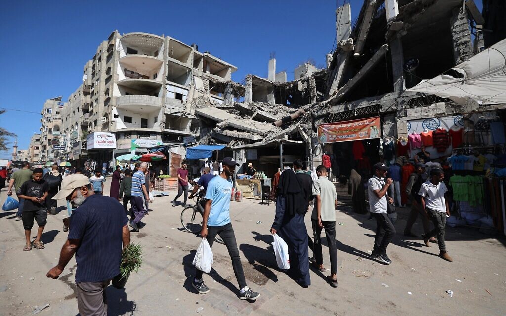 Des Palestiniens passent devant un bâtiment détruit dans un marché improvisé du camp de réfugiés de Nuseirat, situé dans le centre de la bande de Gaza, le 15 octobre 2025. (Crédit :Eyad BABA / AFP)
