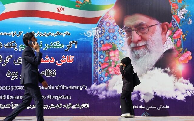 Des Iraniens passent devant une affiche représentant le guide suprême iranien, l'ayatollah Ali Khamenei, à l'extérieur du lieu où se tient la 22e exposition sur les équipements de police et de sécurité, à la mosquée Imam Khomeini de Téhéran, le 15 octobre 2025. (Crédit : ATTA KENARE / AFP)