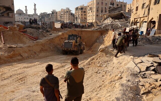 Des gens regardent des Gazaoyus utiliser une excavatrice pour creuser profondément dans le sol, vraisemblablement à la recherche de corps, à Khan Younès, dans le sud de la bande de Gaza, le 17 octobre 2025. (Crédit : Omar al-Qattaa/AFP) Des gens regardent des Gazaoyus utiliser une excavatrice pour creuser profondément dans le sol, vraisemblablement à la recherche de corps, à Khan Younès, dans le sud de la bande de Gaza, le 17 octobre 2025. (Crédit : Omar al-Qattaa/AFP)