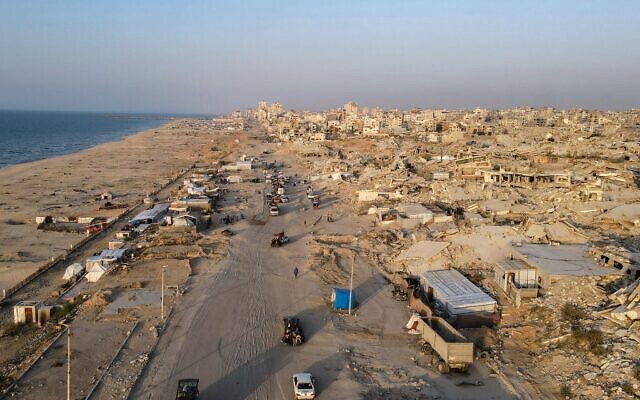 Cette photo aérienne montre des personnes et des véhicules circulant le long de la route Al-Rashid, à côté de bâtiments détruits dans la ville de Gaza, le 23 octobre 2025. (Crédit : AFP)