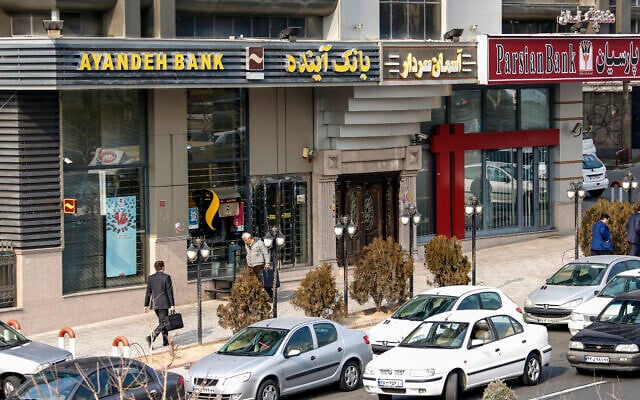 Des Iraniens passent devant une succursale de la banque Ayandeh (à gauche) dans la capitale Téhéran, le 14 janvier 2017. (Crédit :: ATTA KENARE / AFP Des Iraniens passent devant une succursale de la banque Ayandeh (à gauche) dans la capitale Téhéran, le 14 janvier 2017. (Crédit :: ATTA KENARE / AFP