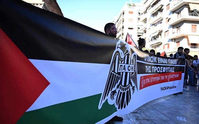 Des manifestants pro-palestiniens brandissent une banderole sur laquelle est écrit : "Le PAOK est l'enfant des réfugiés. Non au déplacement et au génocide" lors d'un rassemblement avant un match de football de la Ligue Europa entre le PAOK et l'équipe israélienne du Maccabi Tel Aviv dans la ville portuaire de Thessalonique, dans le nord de la Grèce, le 24 septembre 2025. (Crédit : AP/Giannis Papanikos)